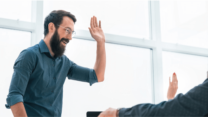 Two colleagues celebrating success with a high-five in a bright office.