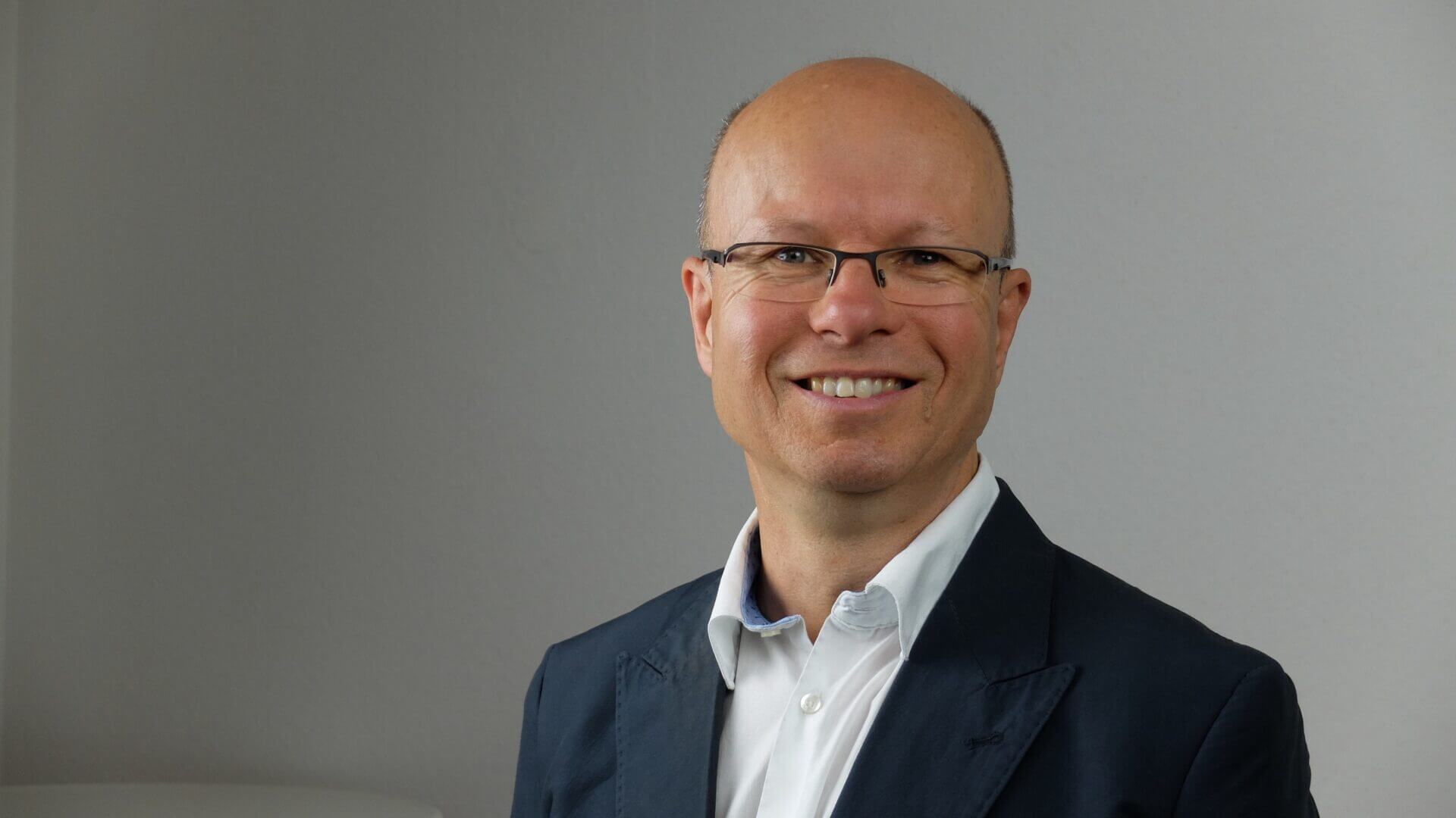Professional trainer and coach smiling in business attire against a neutral background.